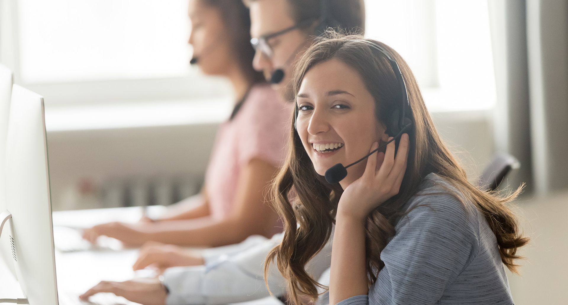 Lächelnde Frau mit Headset, die konzentriert an ihrem Computer arbeitet.